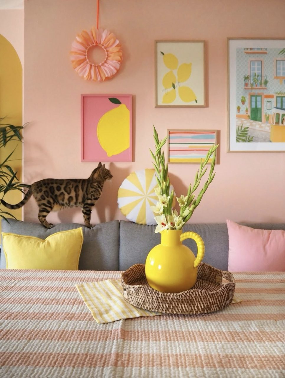 Strukturbild mit Zitronenmotiv auf pinkem Hintergrund. Hängt an einer Wand mit anderen sommerlichen Bildern. Davor steht ein Sofa, auf dem eine Katze sitzt.
