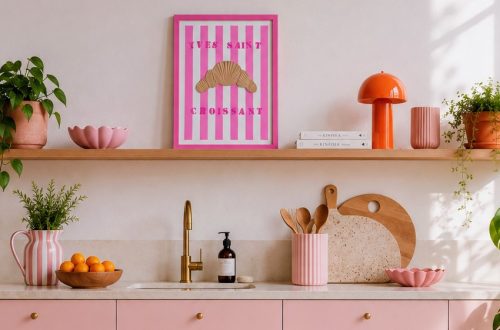 Moderne Küche in hellrose im Scandi Style. Darüber ein Holzregal mit einem Kunstwerk gestreifter Hintergrund in Weiß und Pink mit einem Croissant aus Strukturpaste und der Aufschrift "AYES SAINT CROISSANT".